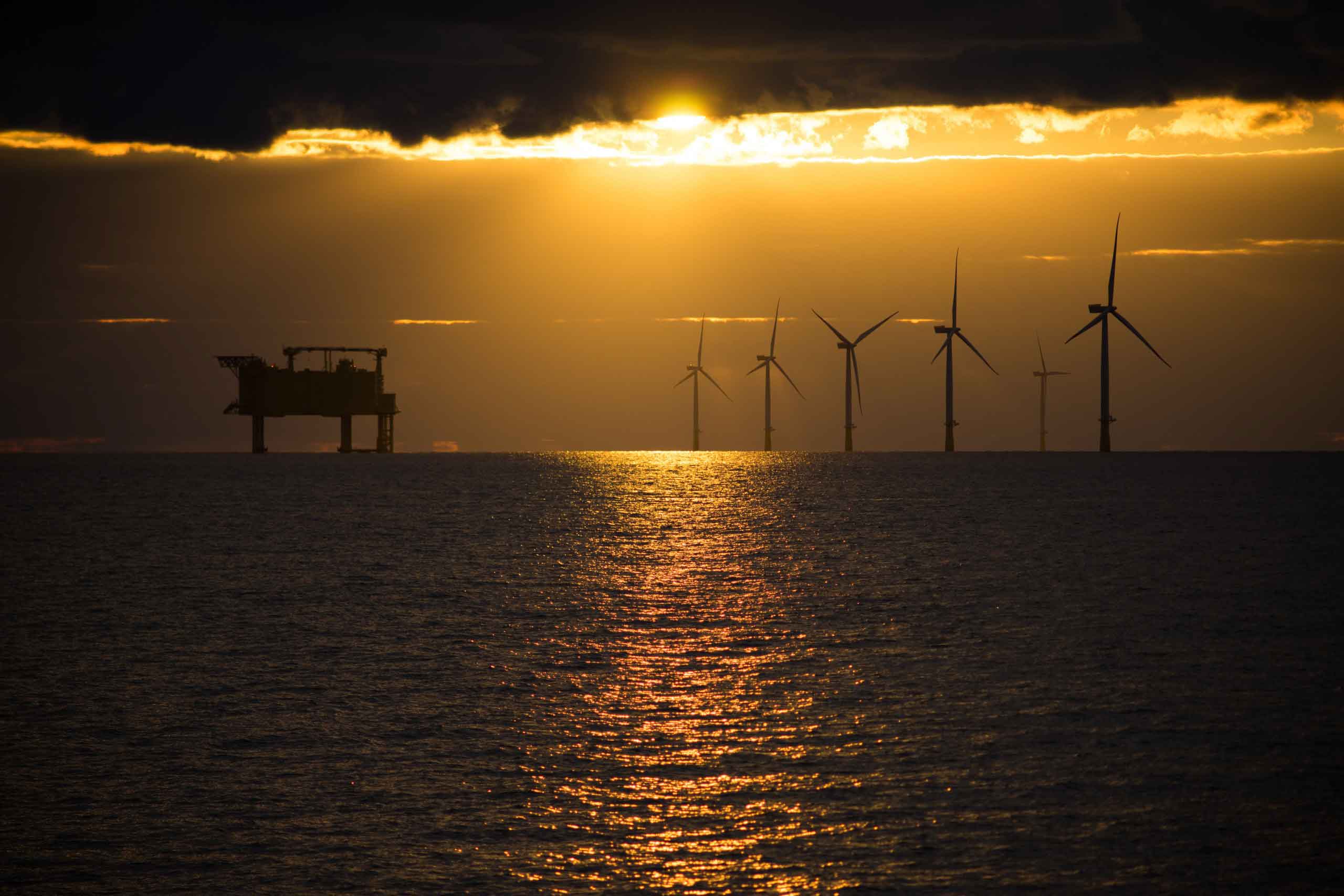 Offshore rig and wind turbines silhouetted against the sunset